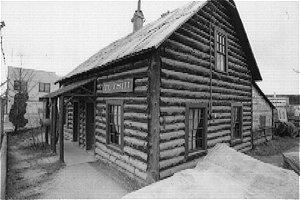 The Telegraph Office is a log building has a steep gable roof and a small covered entry. The roof is covered by corrugated sheet metal and it sits on a wood sill foundation.